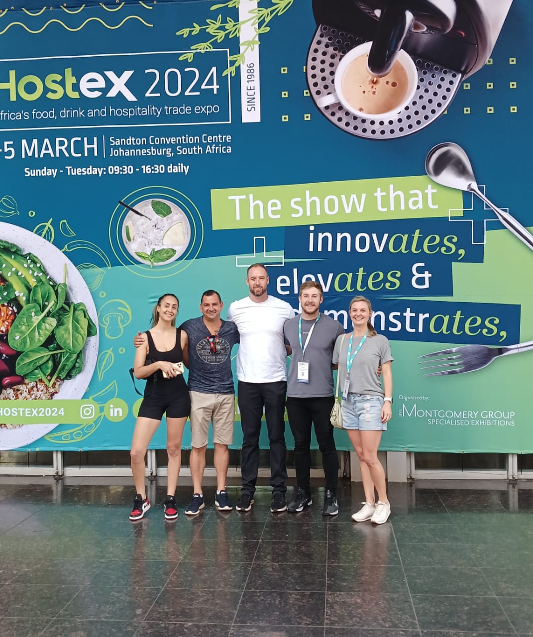 5 people standing in front of a large Hostex 2024 poster